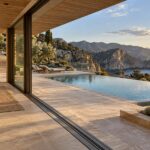 Contemporary coastal residence with a sheltered pale-stone terrace, a grounded infinity pool, and rugged cliffs descending toward the sea.
