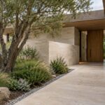 Quiet residential entrance with limestone garden wall, a sheltering oak canopy, graded stone pathway, and planted court.