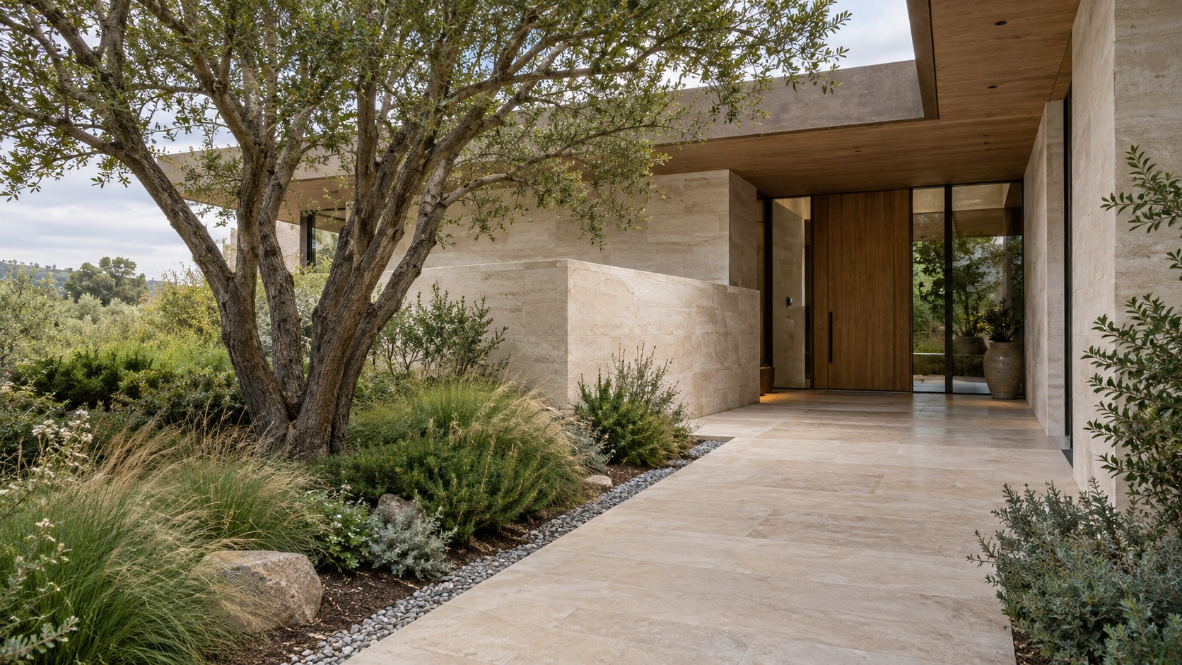 Quiet residential entrance with limestone garden wall, a sheltering oak canopy, graded stone pathway, and planted court.
