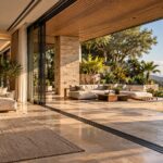 Contemporary tropical living room opening onto a shaded stone terrace and layered garden through broad retractable glazing.
