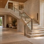 Contemporary limestone entry gallery with a sculptural folded staircase, oak handrail, sheltered garden glazing, and natural daylight.