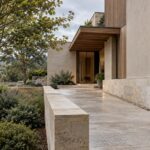 Contemporary limestone residence on a modest raised stone plinth with a sheltered entry, graded path, and planted courtyard.